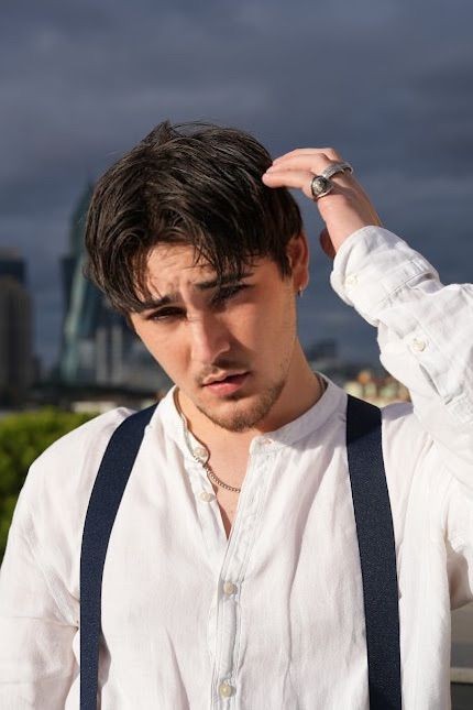 Man in white shirt and suspenders touching his hair with a cityscape background.