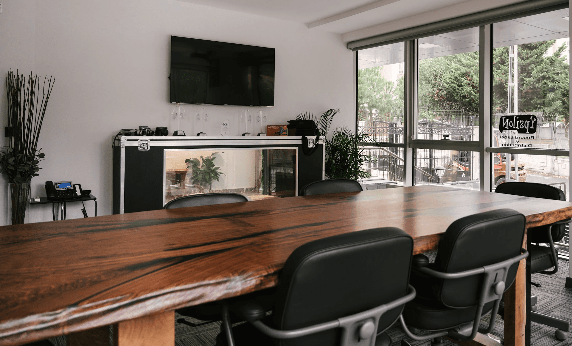 Modern conference room with wooden table, black chairs, plants, and large windows.