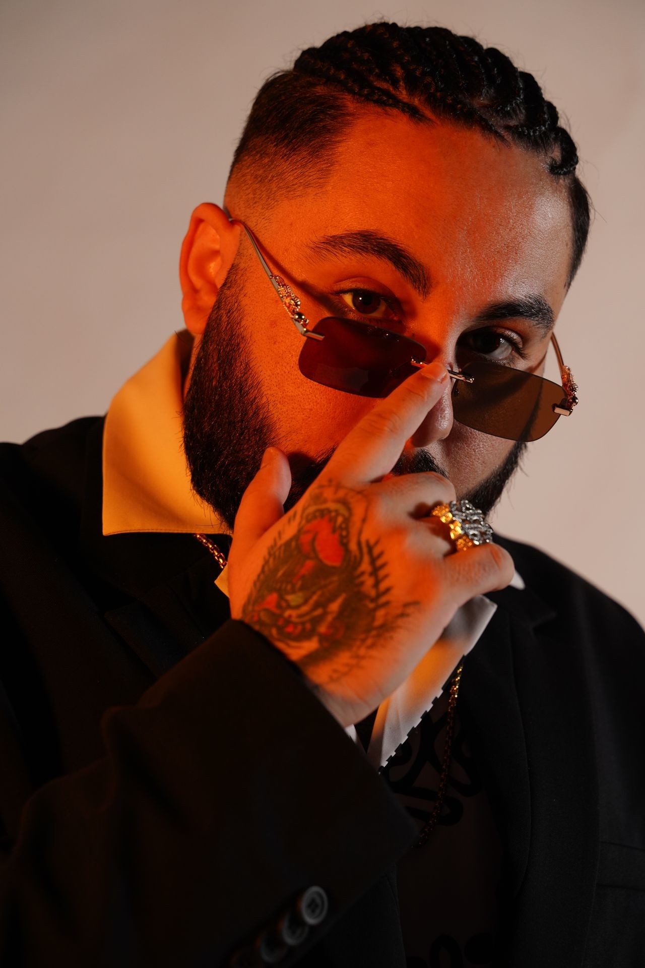 Person with braids and sunglasses, wearing a suit, showing a tattooed hand with rings.